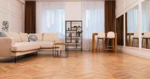 Modern living room with herringbone SPC flooring in Kerala, featuring a light beige sofa, brown curtains, and a minimalist black shelf.